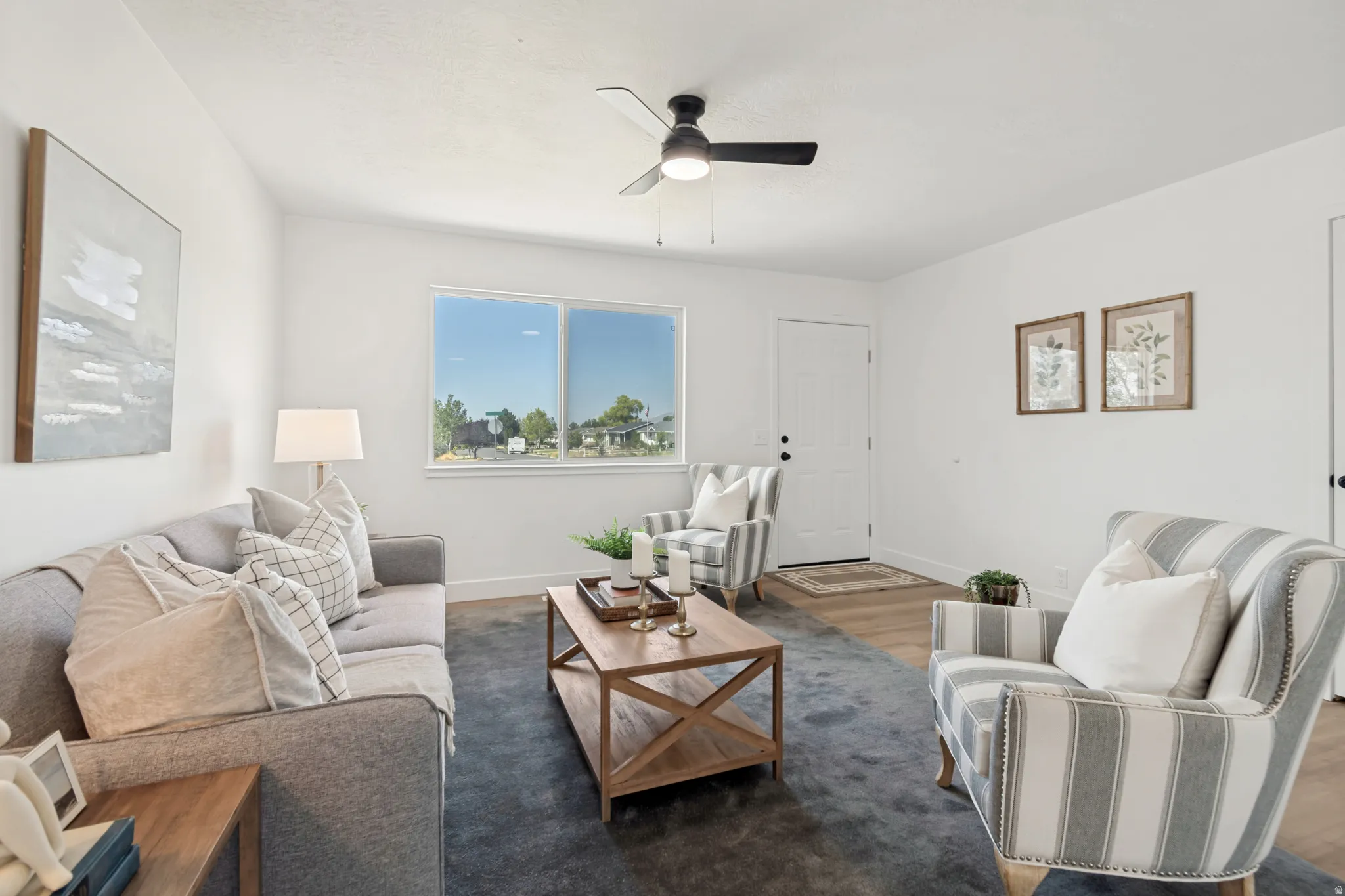 Living area featuring a ceiling fan, a large window, a white door, and wood-finish flooring with a dark area rug