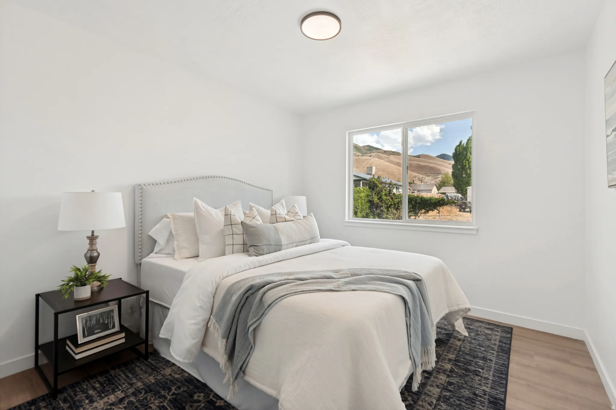 Bright bedroom featuring a large window, wood-finish flooring, white walls, and a recessed ceiling light