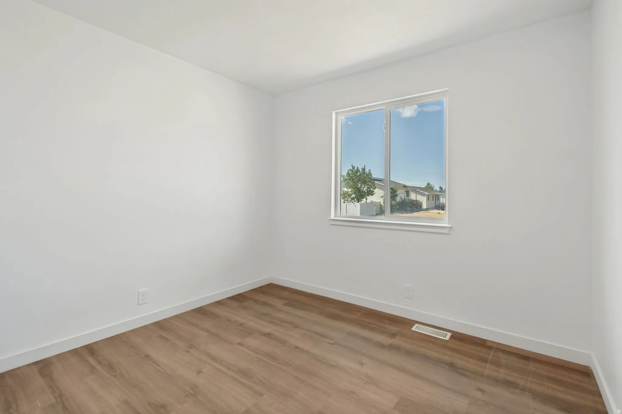 Neutral white walls featuring a single window with white trim, wood-finish flooring, and white baseboards
