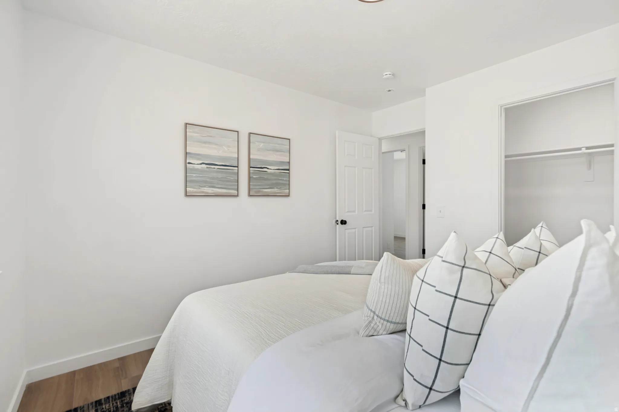 Room featuring light wood-finish flooring, white walls, and a built-in closet with shelving and hanging rod
