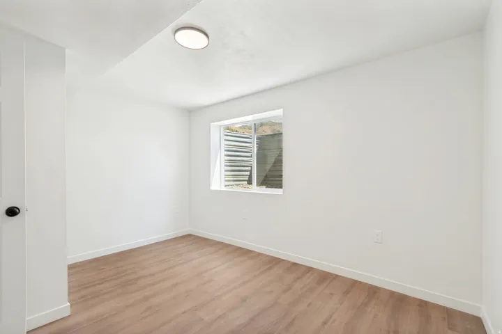 Bright room featuring light wood-finish flooring, white walls, and a single window