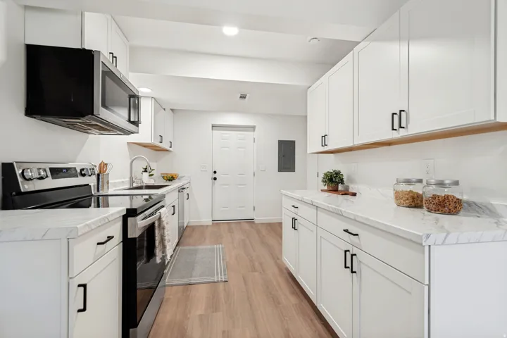 Modern kitchen featuring white shaker cabinetry, stainless steel appliances, marble-look countertops, and wood-finish flooring