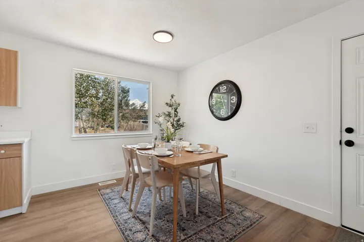 Bright dining area featuring wood-finish flooring, a contemporary flush-mount ceiling light, white baseboards, and a large window providing natural illumination