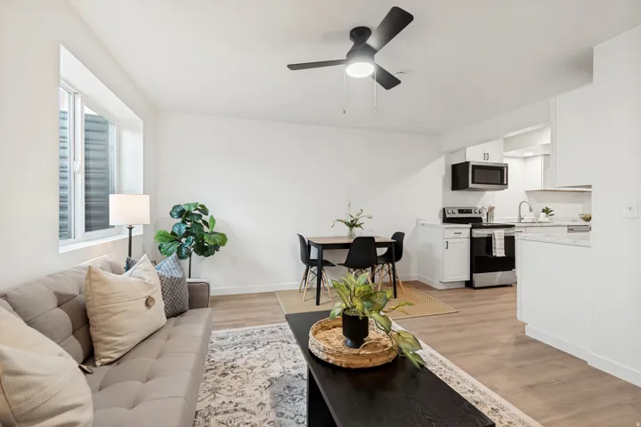 Open-concept living space featuring wood-finish flooring, white walls, and a black ceiling fan