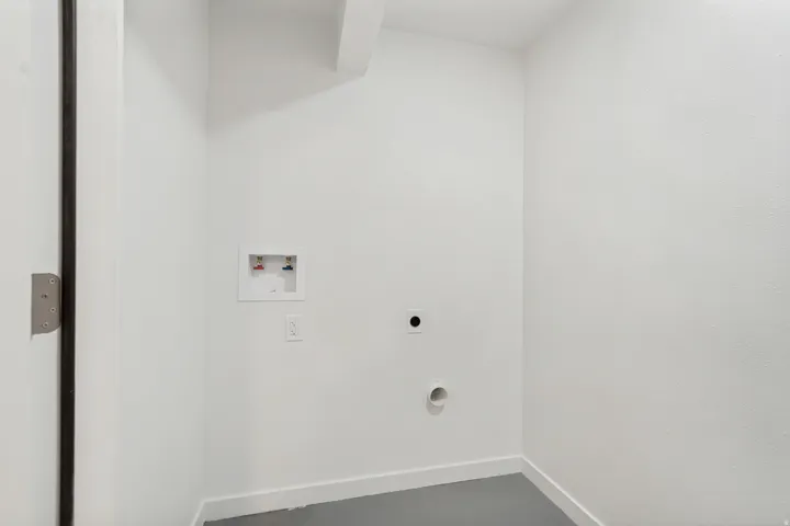 Laundry area featuring a wall-mounted water supply box and dryer vent, with a neutral gray floor and white baseboards