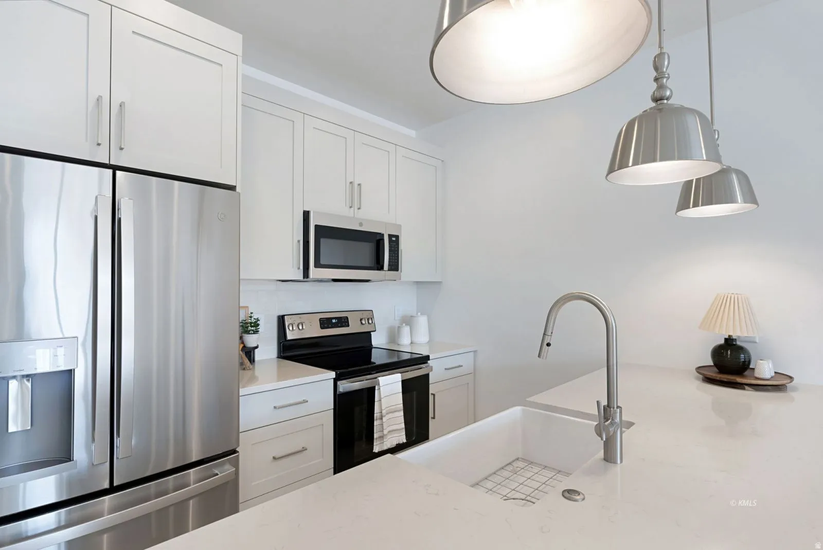 Modern kitchen featuring a large white sink with a gooseneck faucet, light-toned countertops, and white shaker-style cabinetry