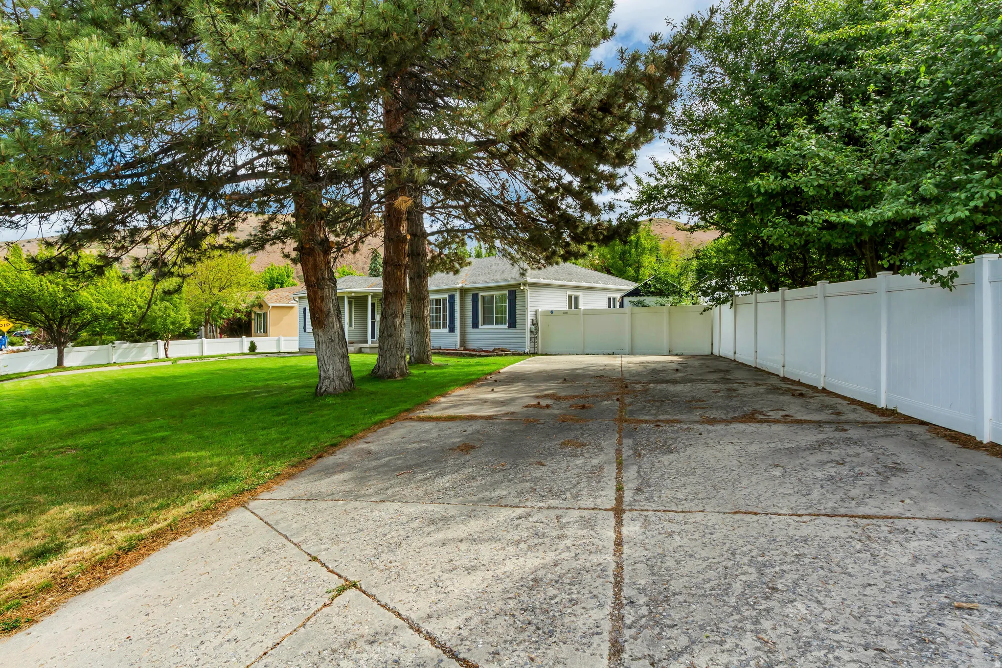 Expansive concrete driveway featuring a white vinyl privacy fence along one side