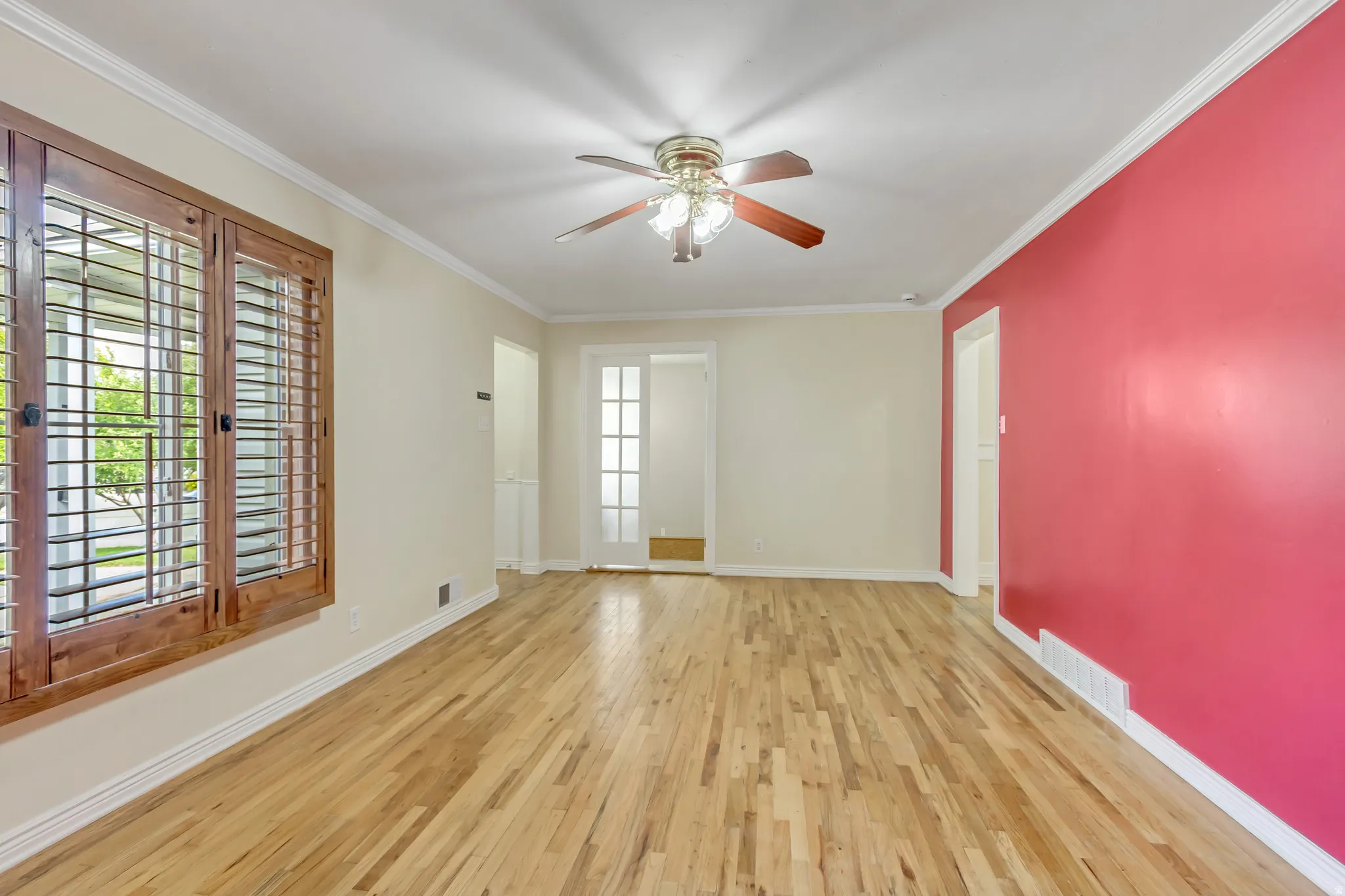 Spacious interior featuring wood-finish flooring, a ceiling fan with integrated lighting, crown molding, and a solid wood plantation shutter window