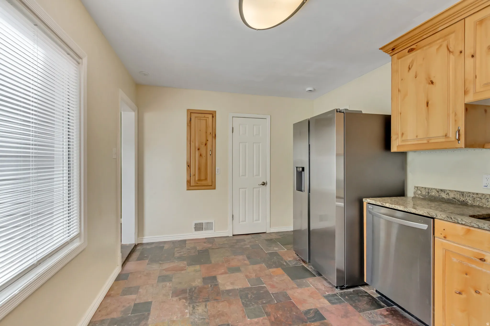 Kitchen featuring a multi-tone tile floor, wood cabinetry, granite countertops, and stainless steel appliances