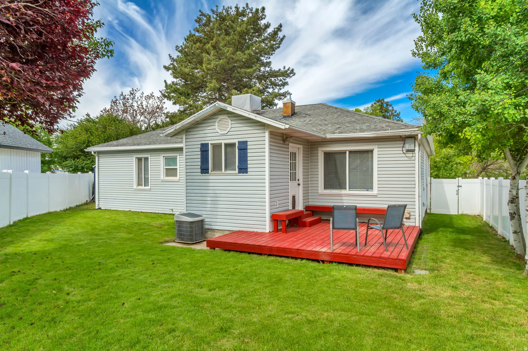 Spacious backyard featuring a vibrant red deck, manicured lawn, and white privacy fencing