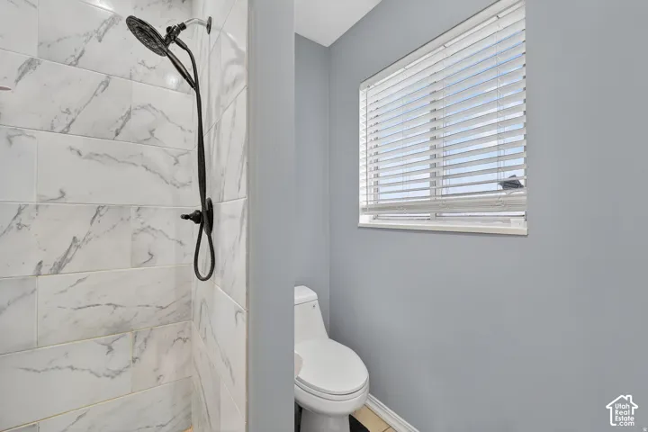 Shower with a black matte multi-function showerhead, white marble-look subway tile surround, and neutral wall paint