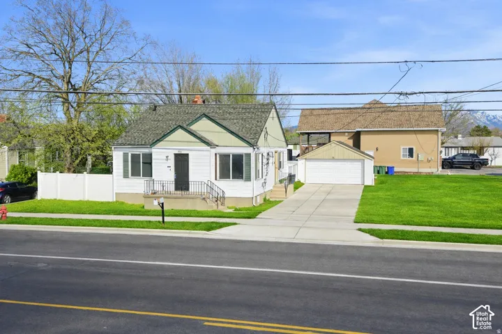 White exterior with green gables, featuring a covered entry porch with iron railings, a two-car detached garage, and a concrete driveway