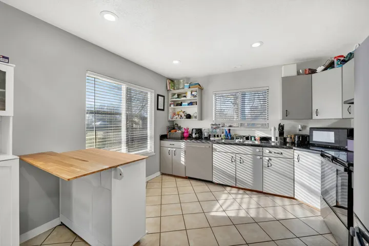 Kitchen featuring tile flooring, white cabinetry, dark countertops, recessed lighting, and a double window with horizontal blinds