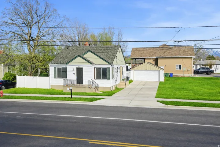 White exterior with green gables, featuring a covered entry porch with iron railings, a two-car detached garage, and a concrete driveway