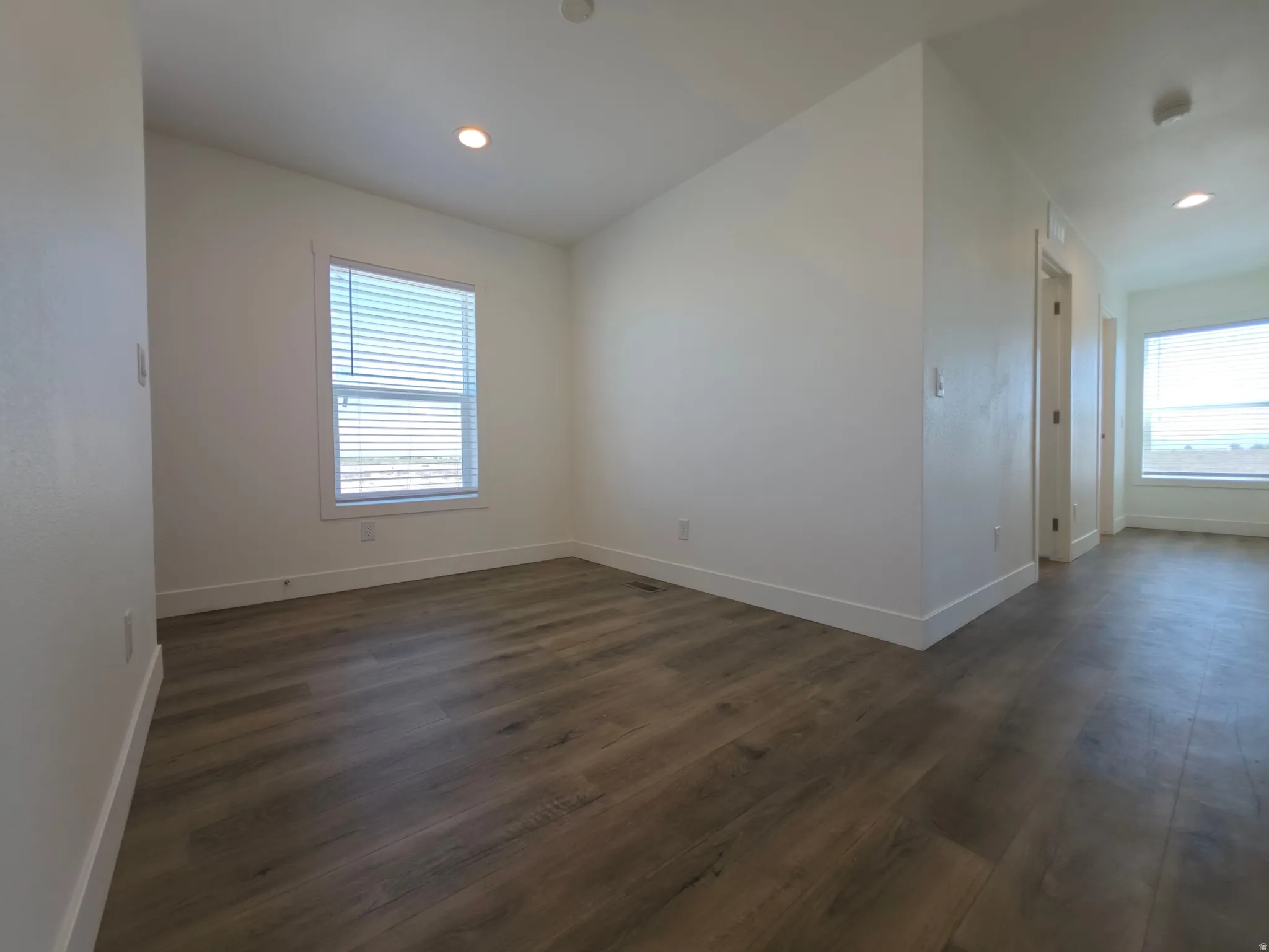 Bright room featuring wood-finish flooring, recessed lighting, white walls, and a window with horizontal blinds
