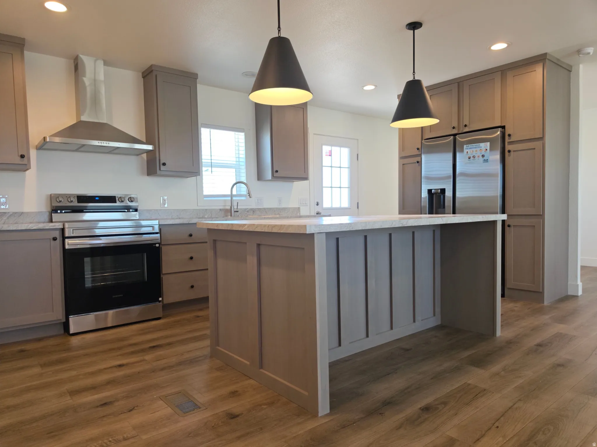 Kitchen featuring an island with shiplap-style detailing, wood-finish flooring, stainless steel appliances, grey cabinetry, and recessed and pendant lighting