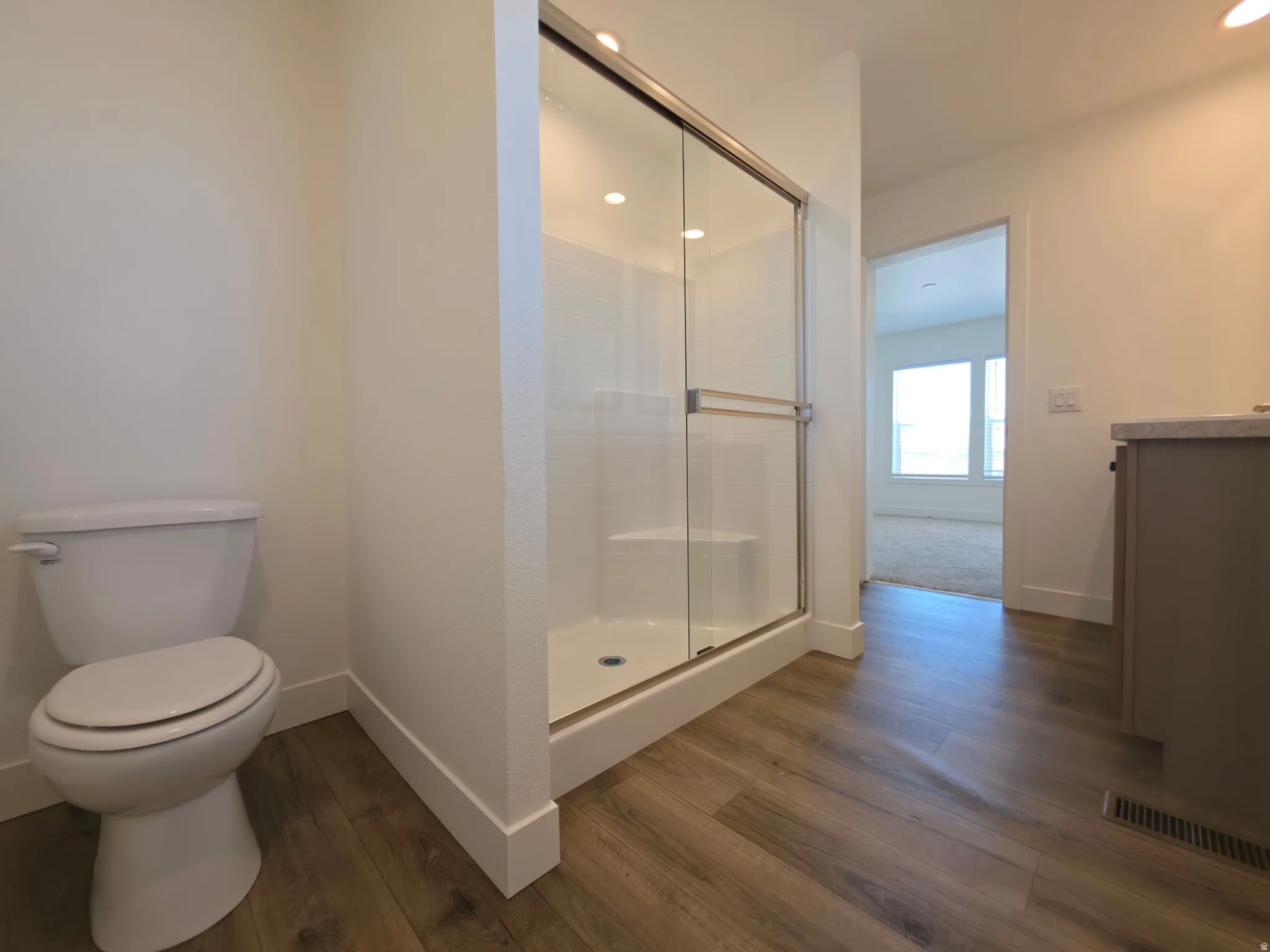 Bathroom featuring wood-finish flooring, a white toilet, and a glass-enclosed shower with a built-in bench