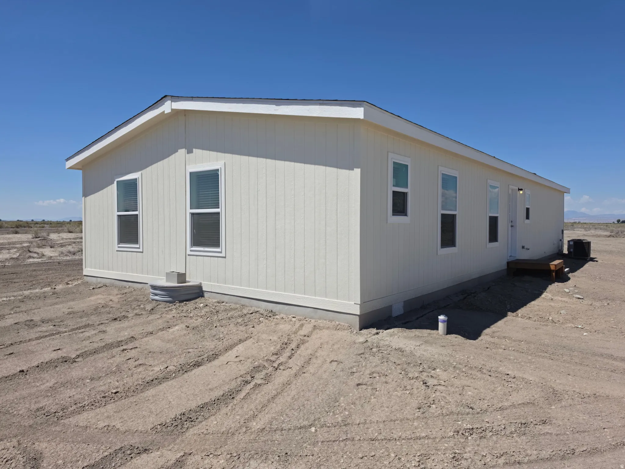 Newly constructed residence featuring light-colored vertical siding, white window trim, a dark asphalt shingle roof, a small wooden step, and visible utility connections