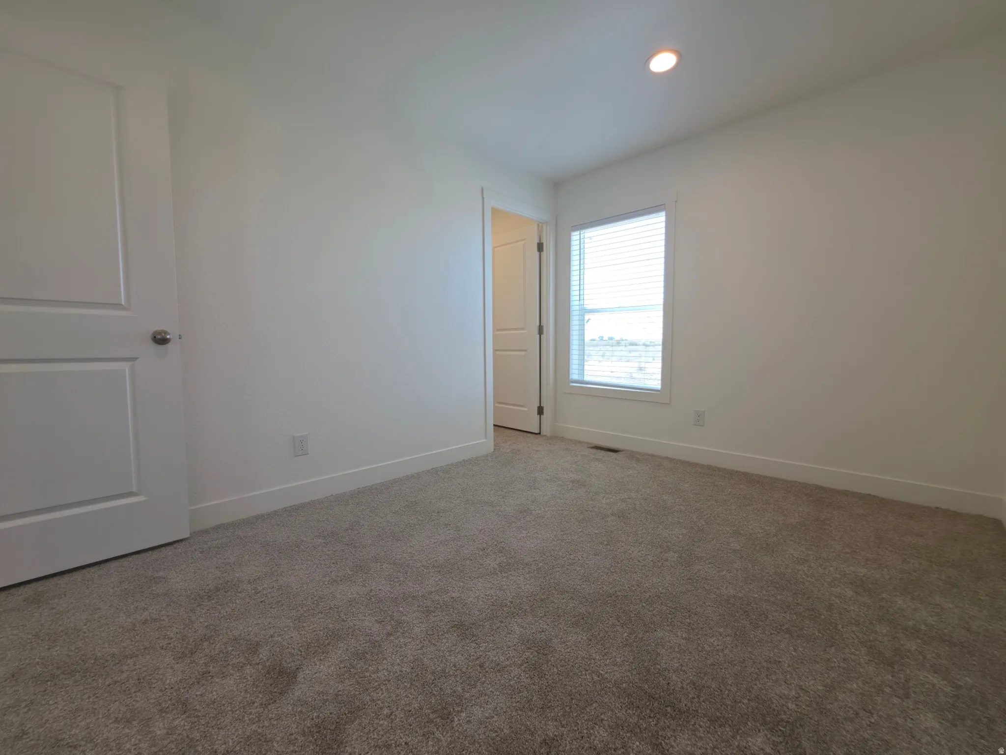 Carpeted interior room featuring a window with horizontal blinds, a white paneled door, a recessed ceiling light, and baseboard trim