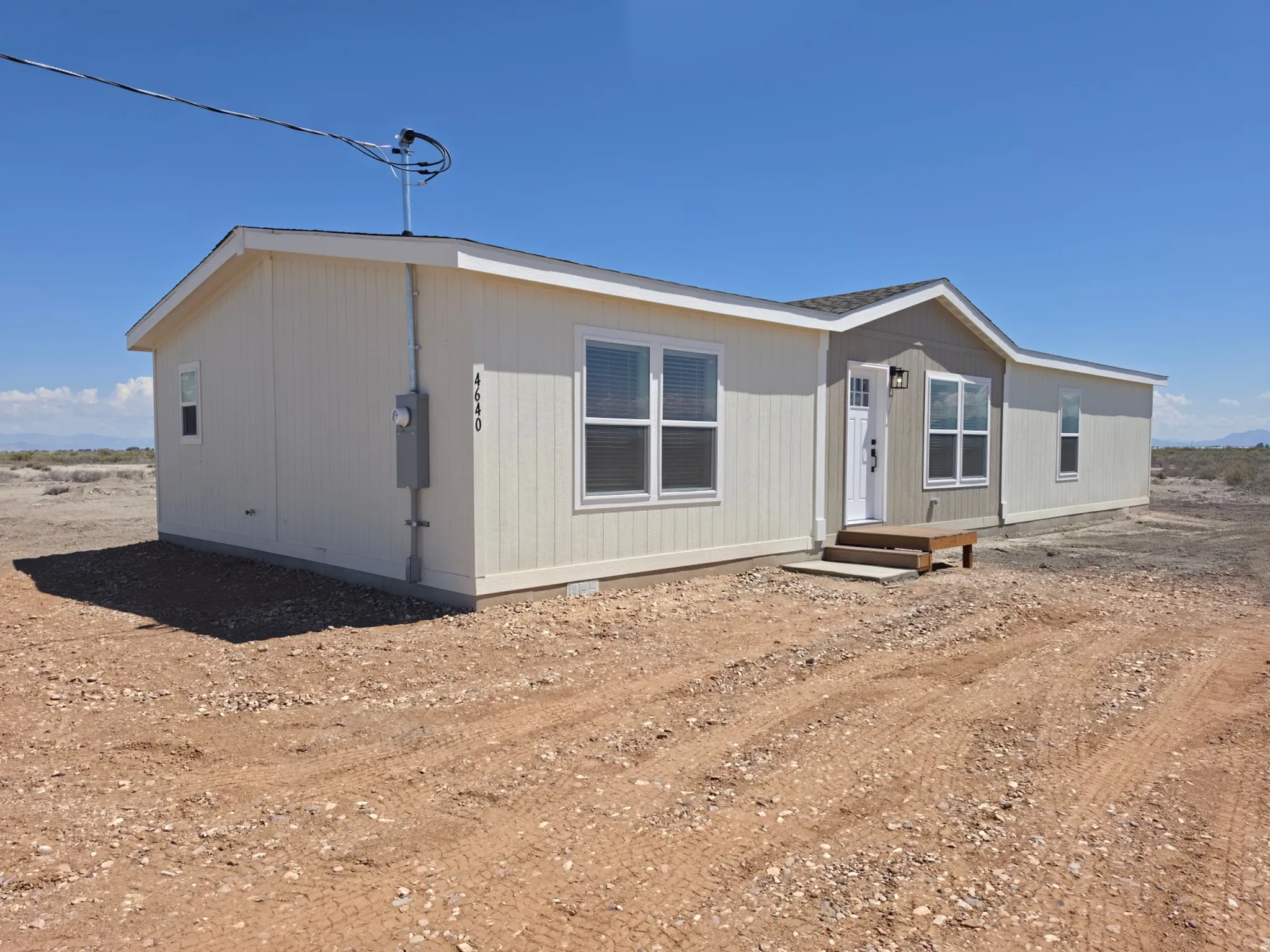 Modern single-story residence featuring light beige vertical siding and a complementary grey gable accent