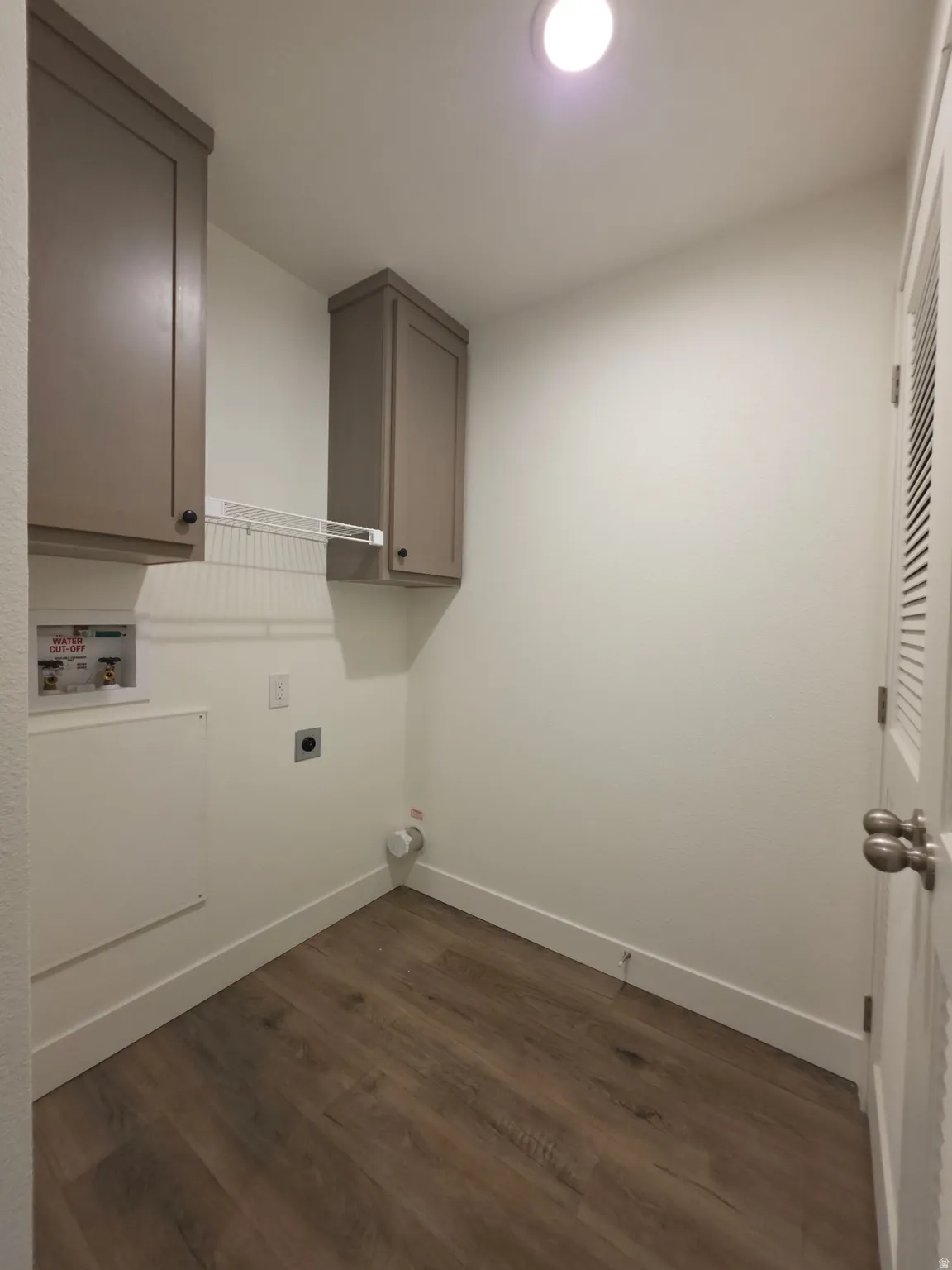 Dedicated laundry area featuring wood-finish flooring, white baseboards, and neutral wall paint