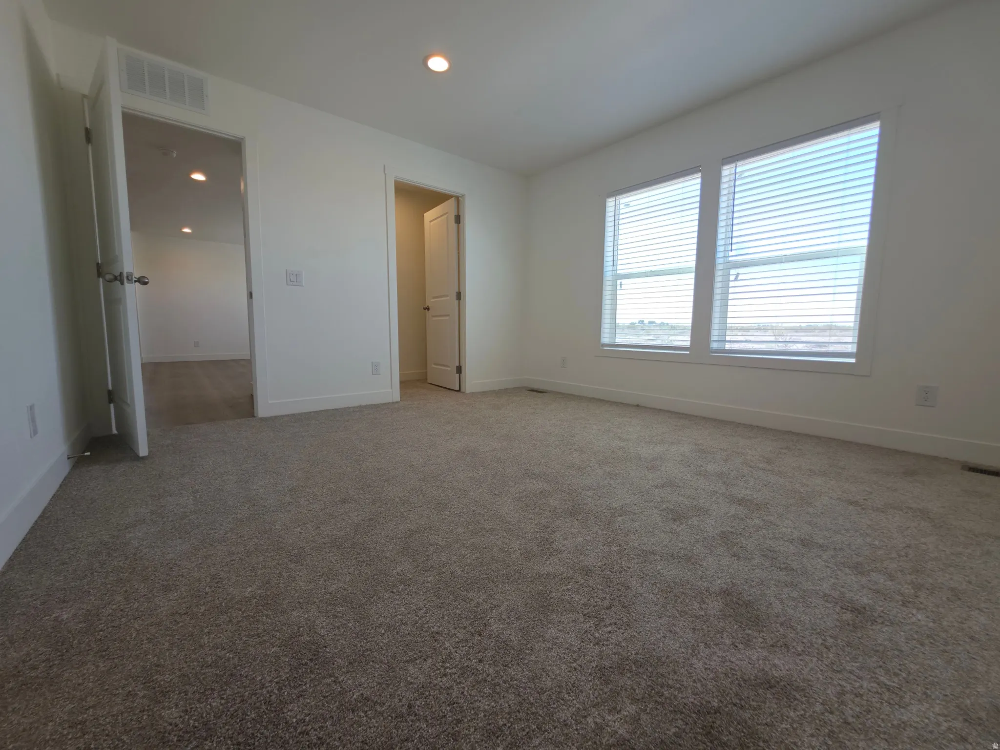Carpeted room featuring two prominent windows with blinds, recessed lighting, and white trim