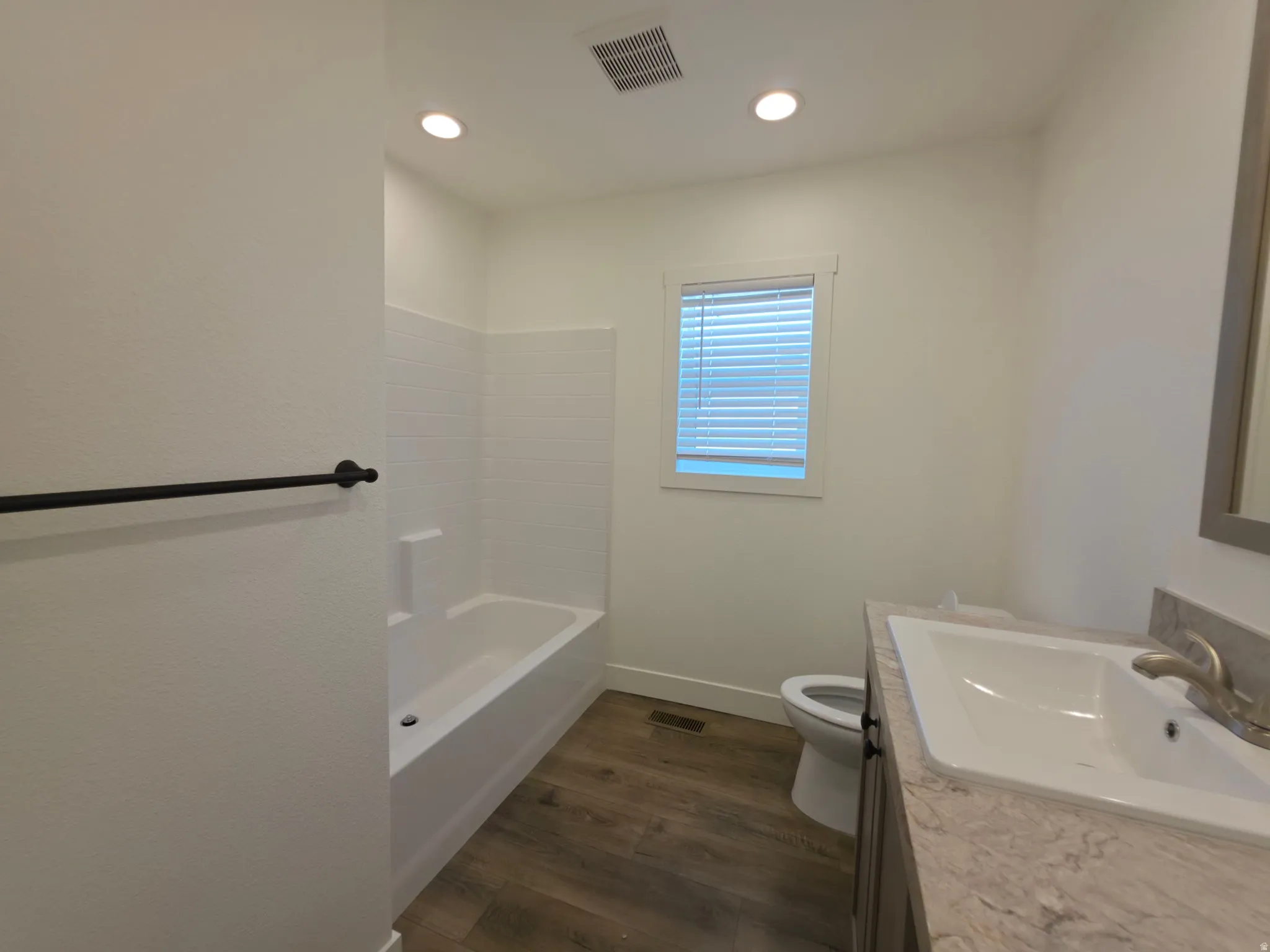 Full bathroom featuring a white tub/shower combination with subway tile surround, wood-finish flooring, a single vanity with a light-toned countertop, and recessed lighting