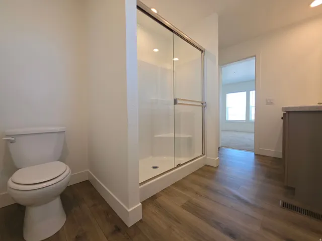 Bathroom featuring wood-finish flooring, a white toilet, and a glass-enclosed shower with a built-in bench