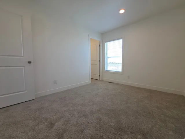Carpeted interior room featuring a window with horizontal blinds, a white paneled door, a recessed ceiling light, and baseboard trim