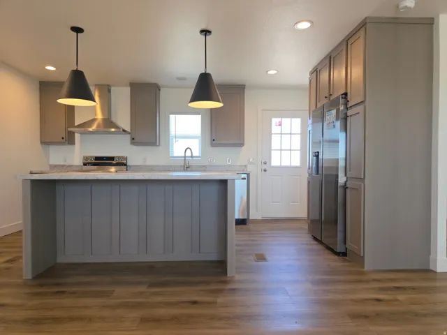 Contemporary kitchen featuring an island with pendant lighting, stainless steel appliances, stone-finish countertops, and wood-finish flooring