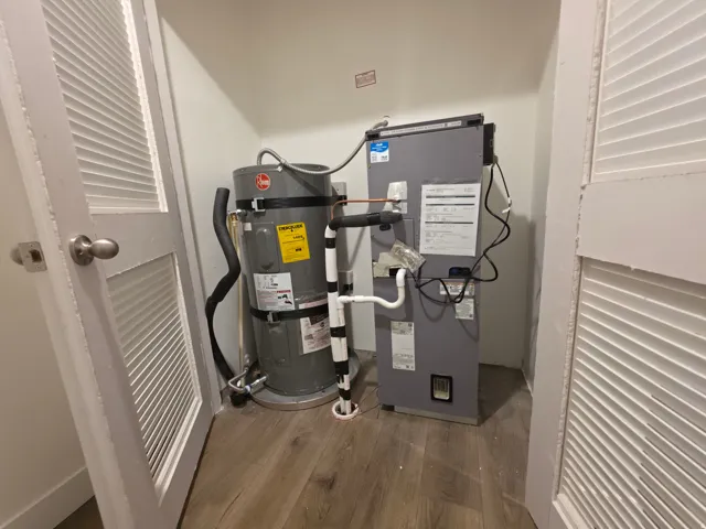 Utility closet featuring water heater and air handler unit, hard surface flooring, and louvered bifold doors