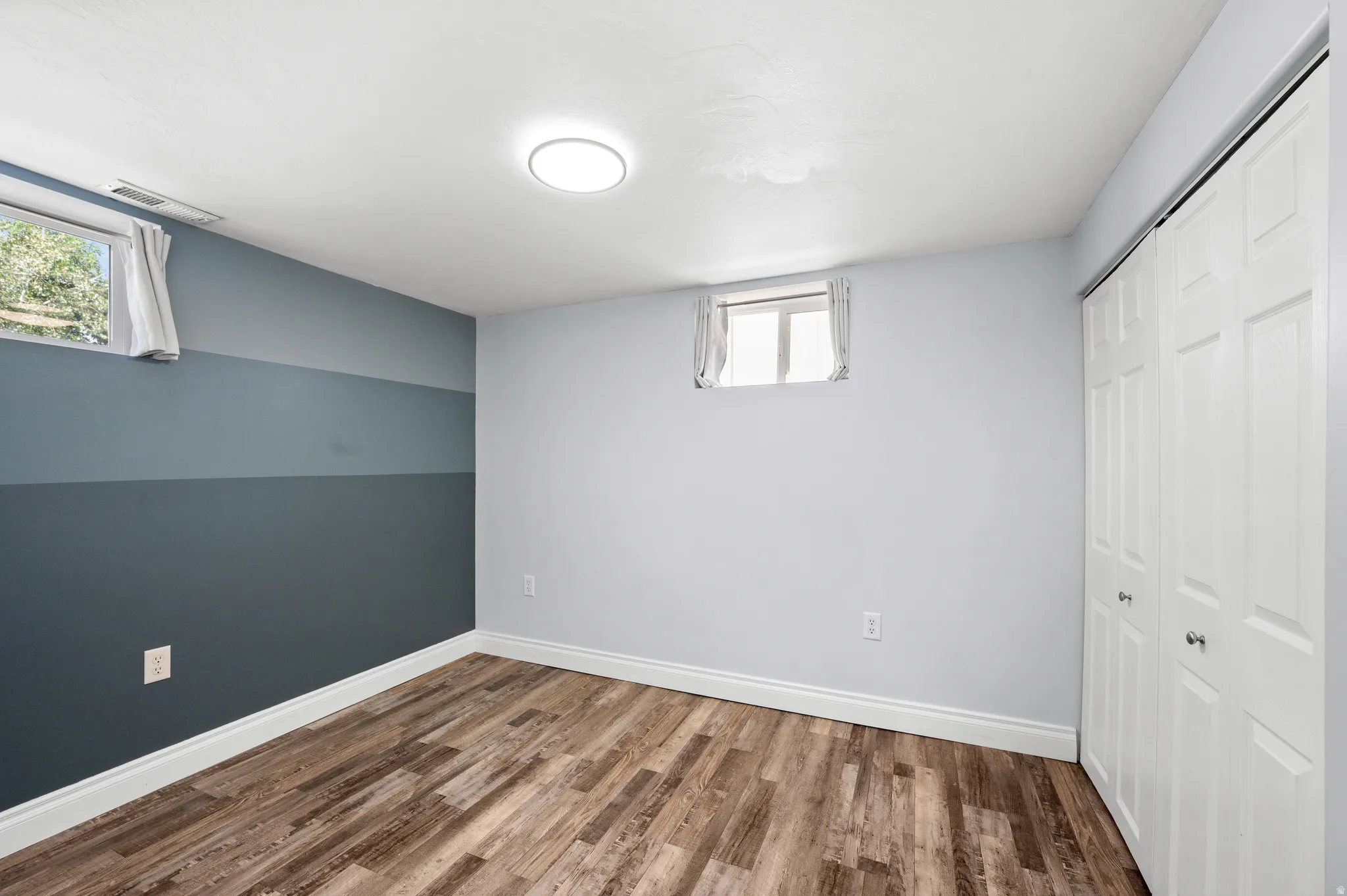 Room featuring wood-finish flooring, two windows, and a built-in bi-fold closet