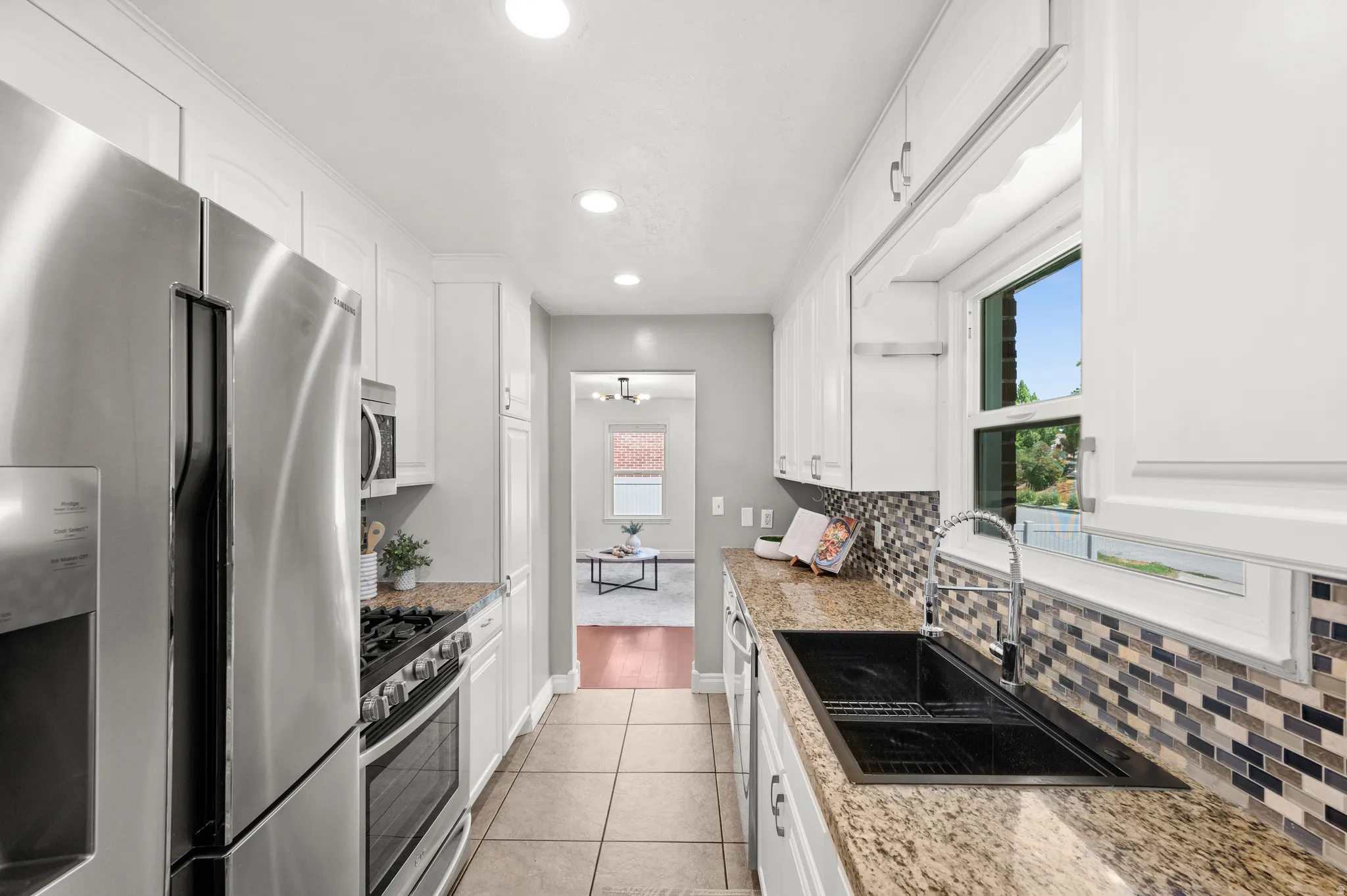 Galley kitchen featuring white cabinetry, recessed lighting, stainless steel appliances, granite-finish countertops, and a mosaic tile backsplash