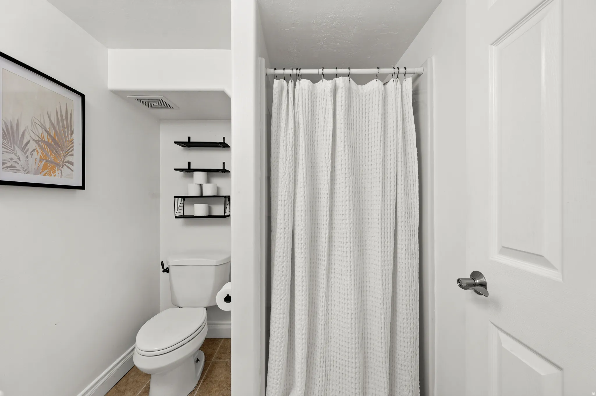 Full bathroom featuring a shower with privacy curtain, white toilet, and tile flooring