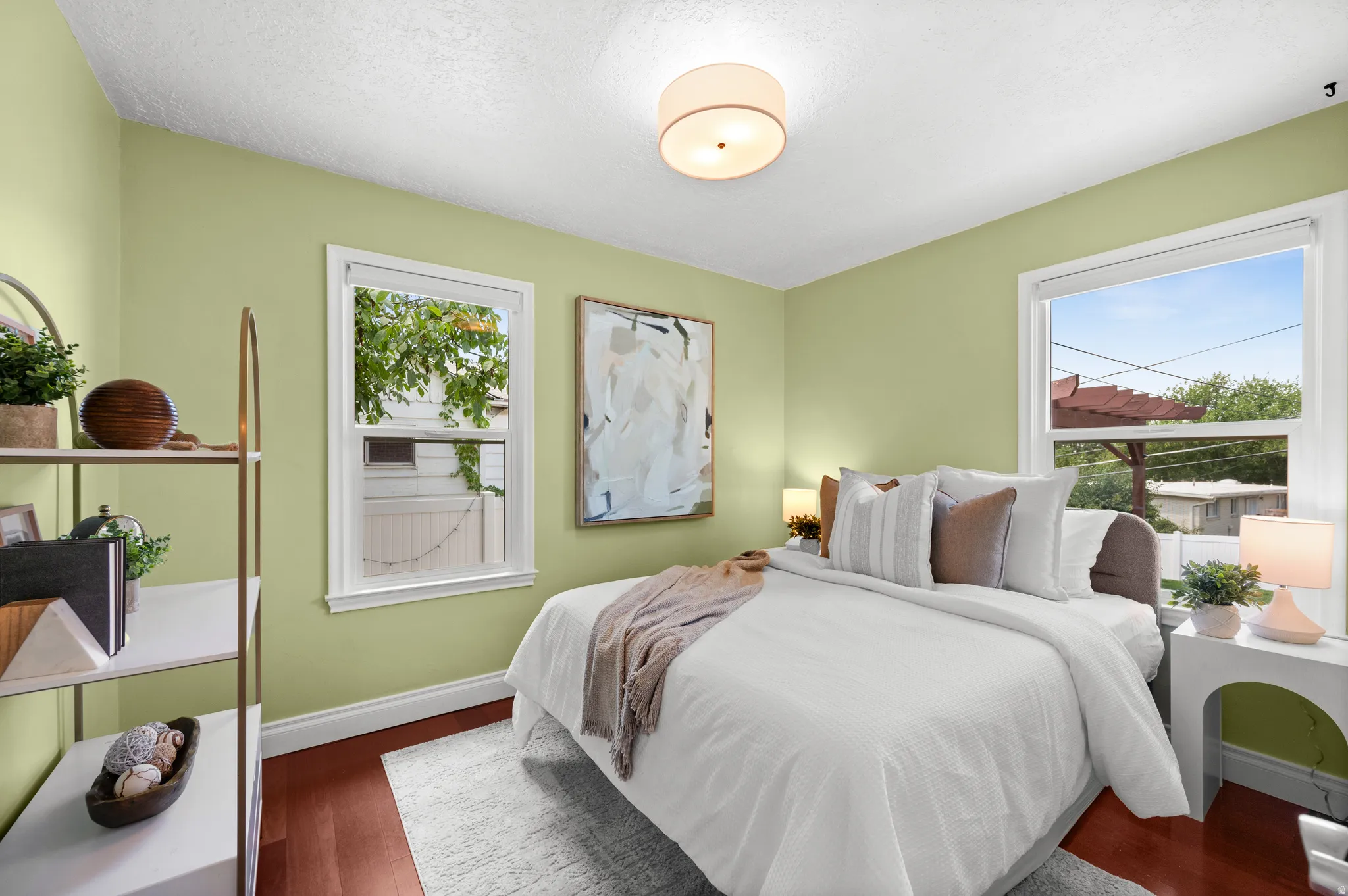 Bedroom featuring light green walls, wood-finish flooring, two windows with white trim, and a ceiling-mounted light fixture