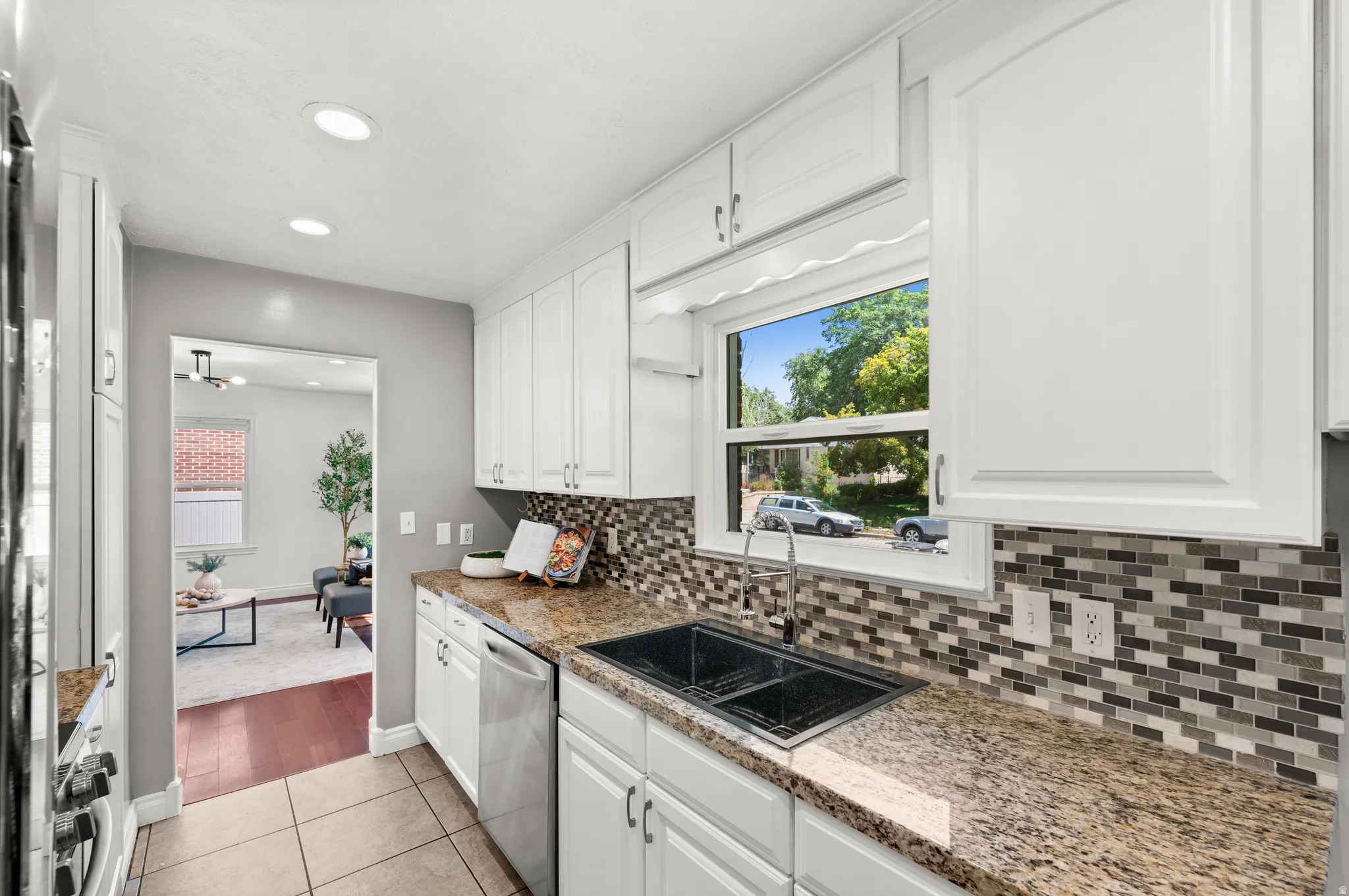 Kitchen featuring white cabinetry, granite countertops, a mosaic tile backsplash, and a double basin sink