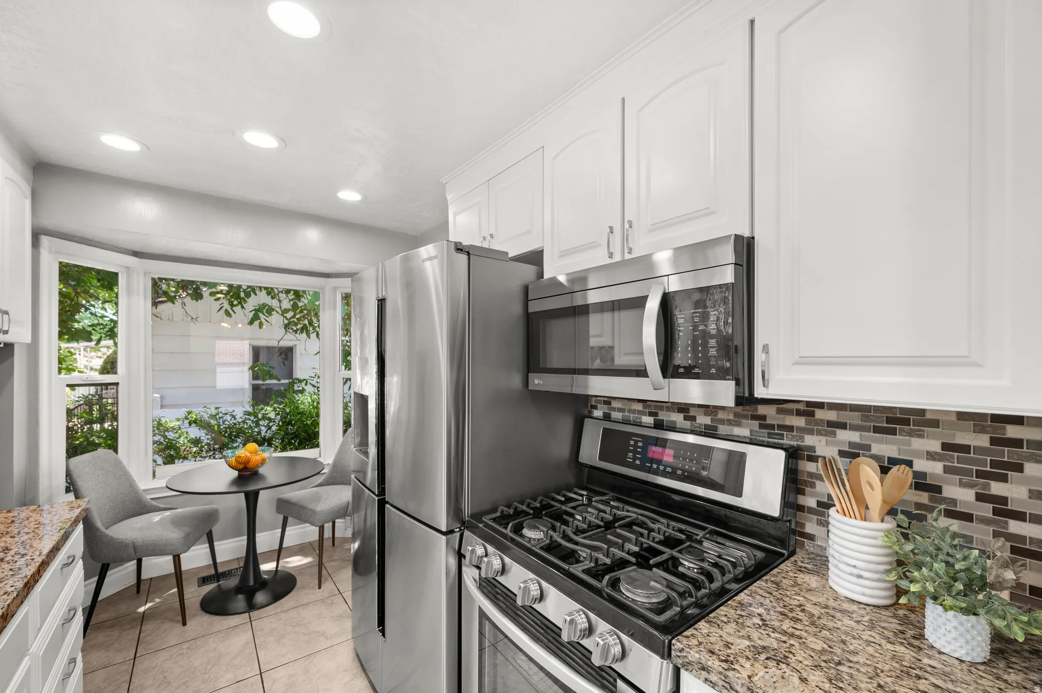 Kitchen featuring a bay window, white cabinetry, recessed lighting, stainless steel appliances, and granite countertops with a mosaic tile backsplash