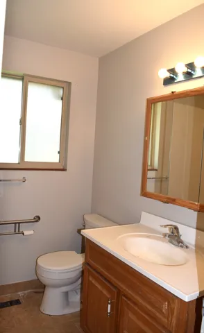 Bathroom featuring a wood-finish vanity with an integrated sink, a large mirror with a coordinating wood-finish frame, and a multi-bulb vanity light fixture