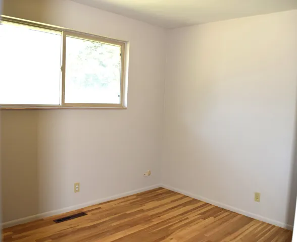 Room featuring wood-finish flooring, white baseboards, and a single window with a light-toned frame