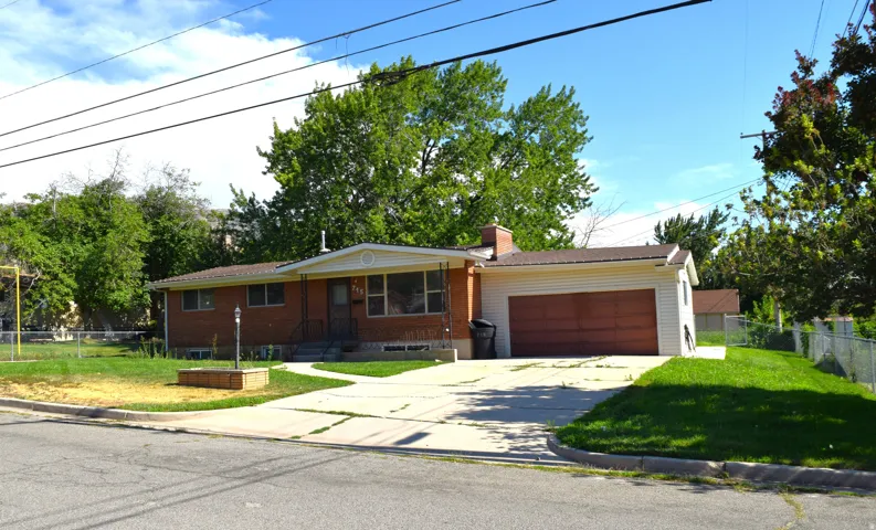 Brick exterior with an attached garage, featuring a paved driveway, front lawn, and mature trees