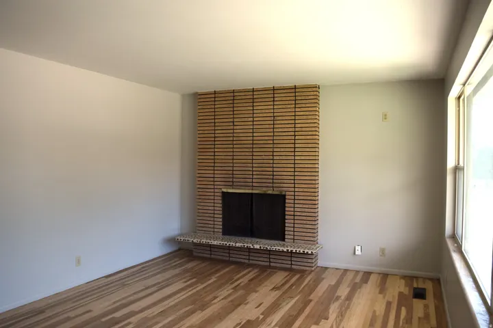 Living area featuring a brick fireplace with a stone hearth, wood-finish flooring, and large windows