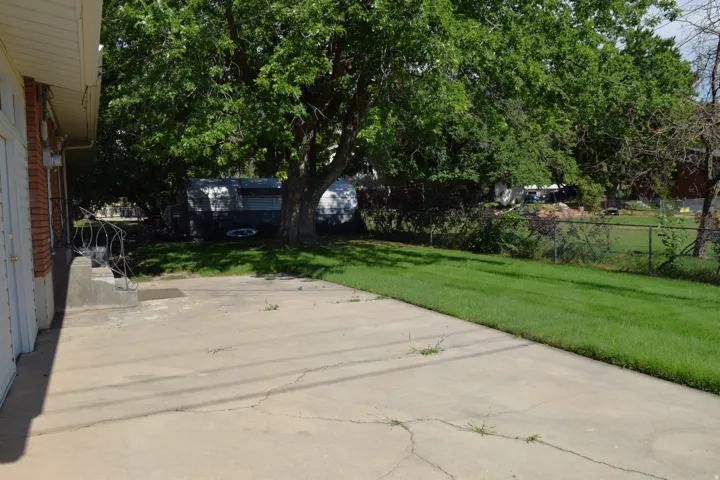 Expansive concrete patio with direct access to a grassy yard featuring mature trees