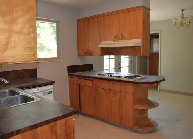 Kitchen featuring a built-in cooktop, integrated dishwasher, double basin sink, wood-finish cabinetry, and dark-toned countertops