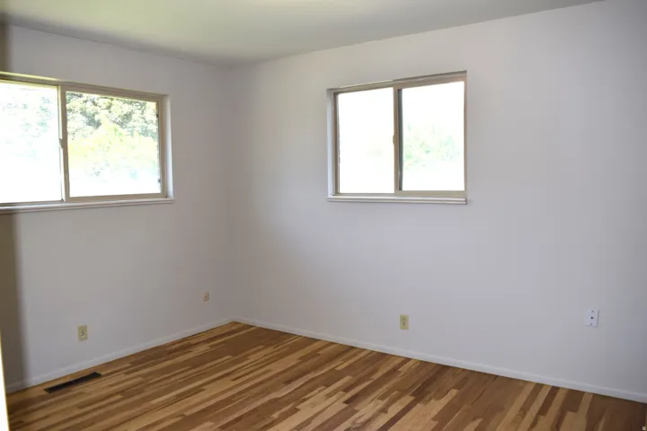 Room featuring wood-finish flooring, two windows, white walls, and white trim