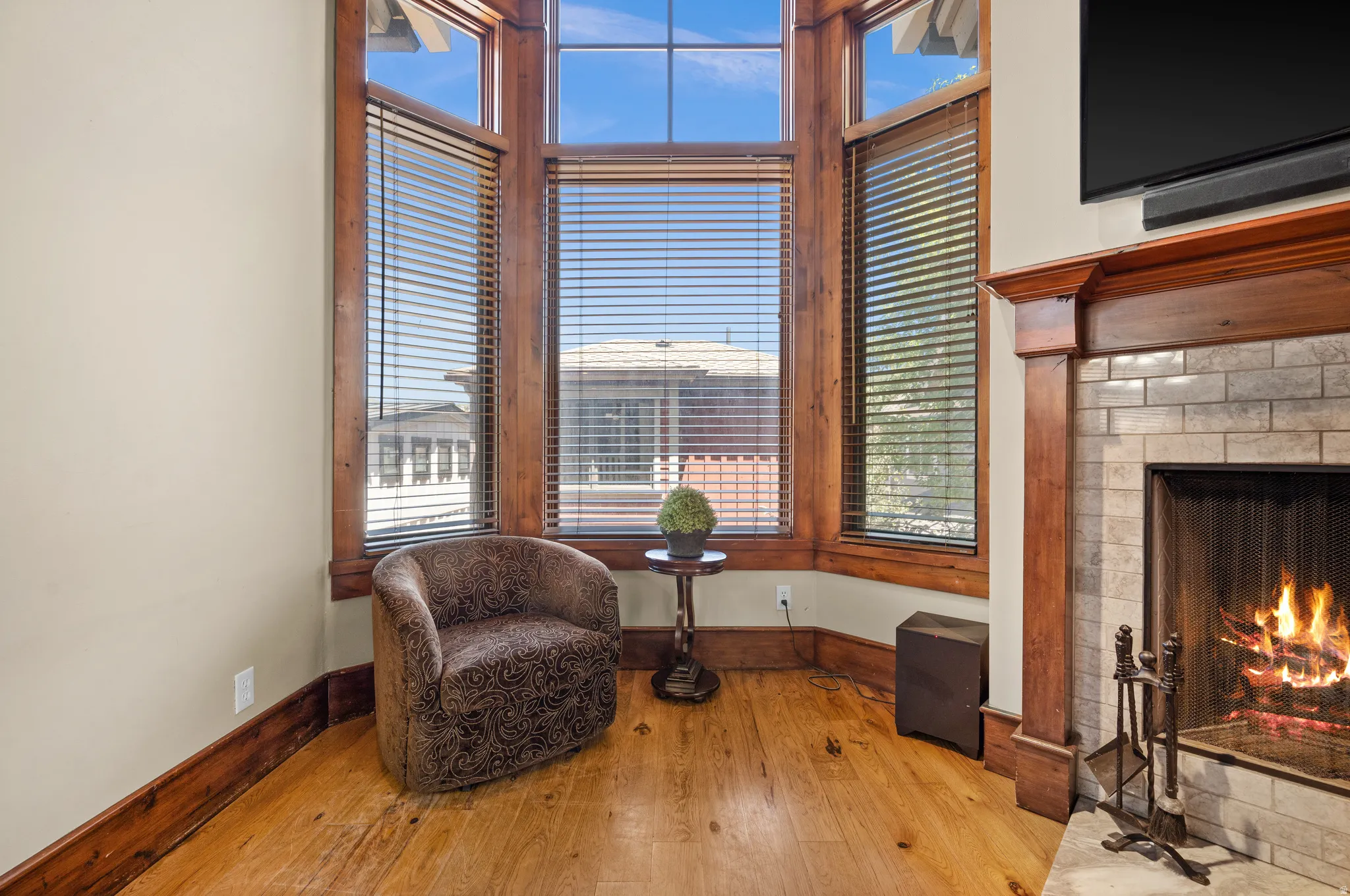 Bay window with wood-finish trim, wood-finish flooring, and a fireplace with a light-colored brick surround