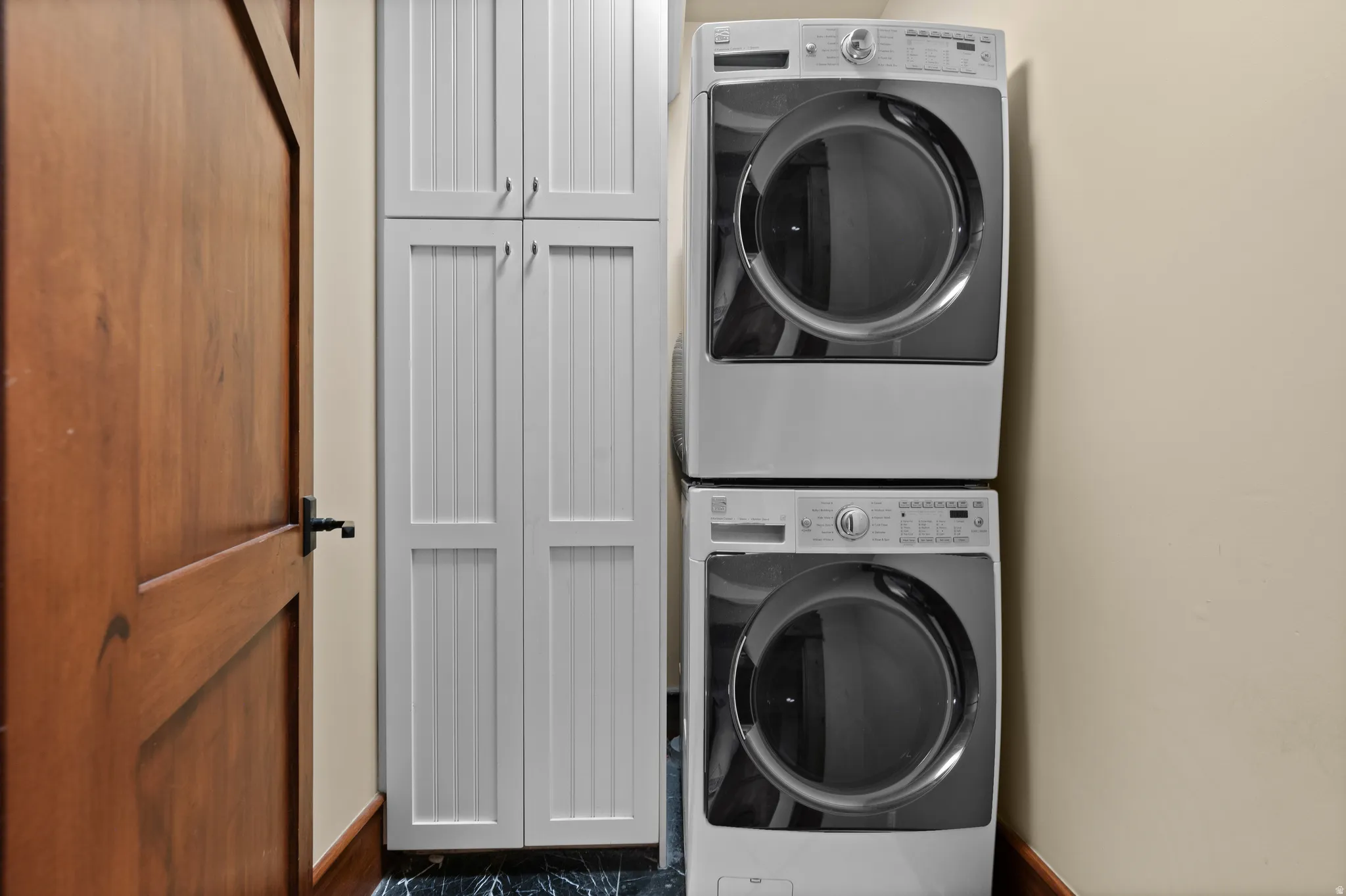 Laundry area featuring a stackable washer and dryer, beadboard cabinetry, a wooden door with dark hardware, and dark flooring