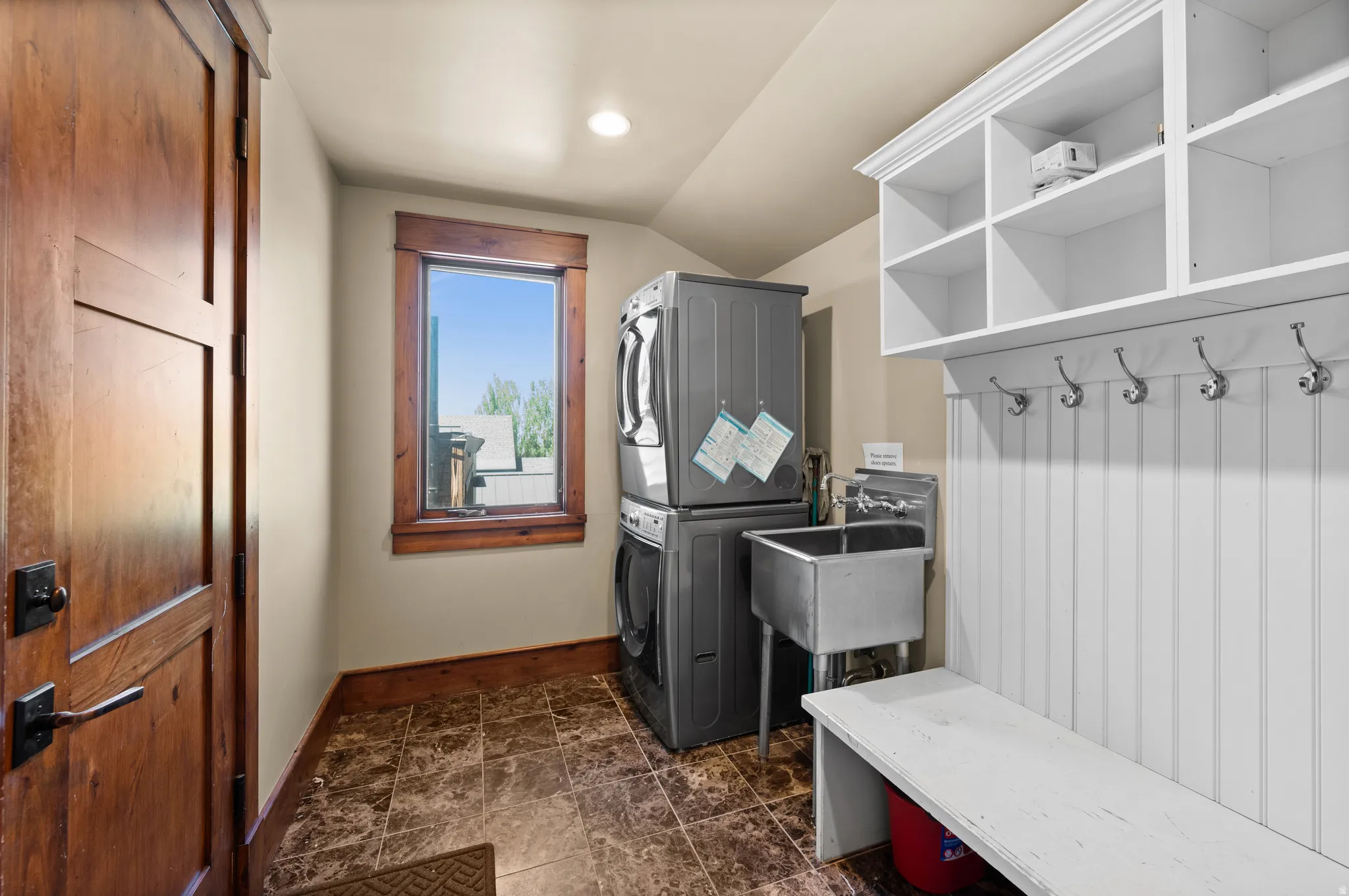 Dedicated utility room featuring stacked laundry appliances, a stainless steel utility sink, and durable tile flooring