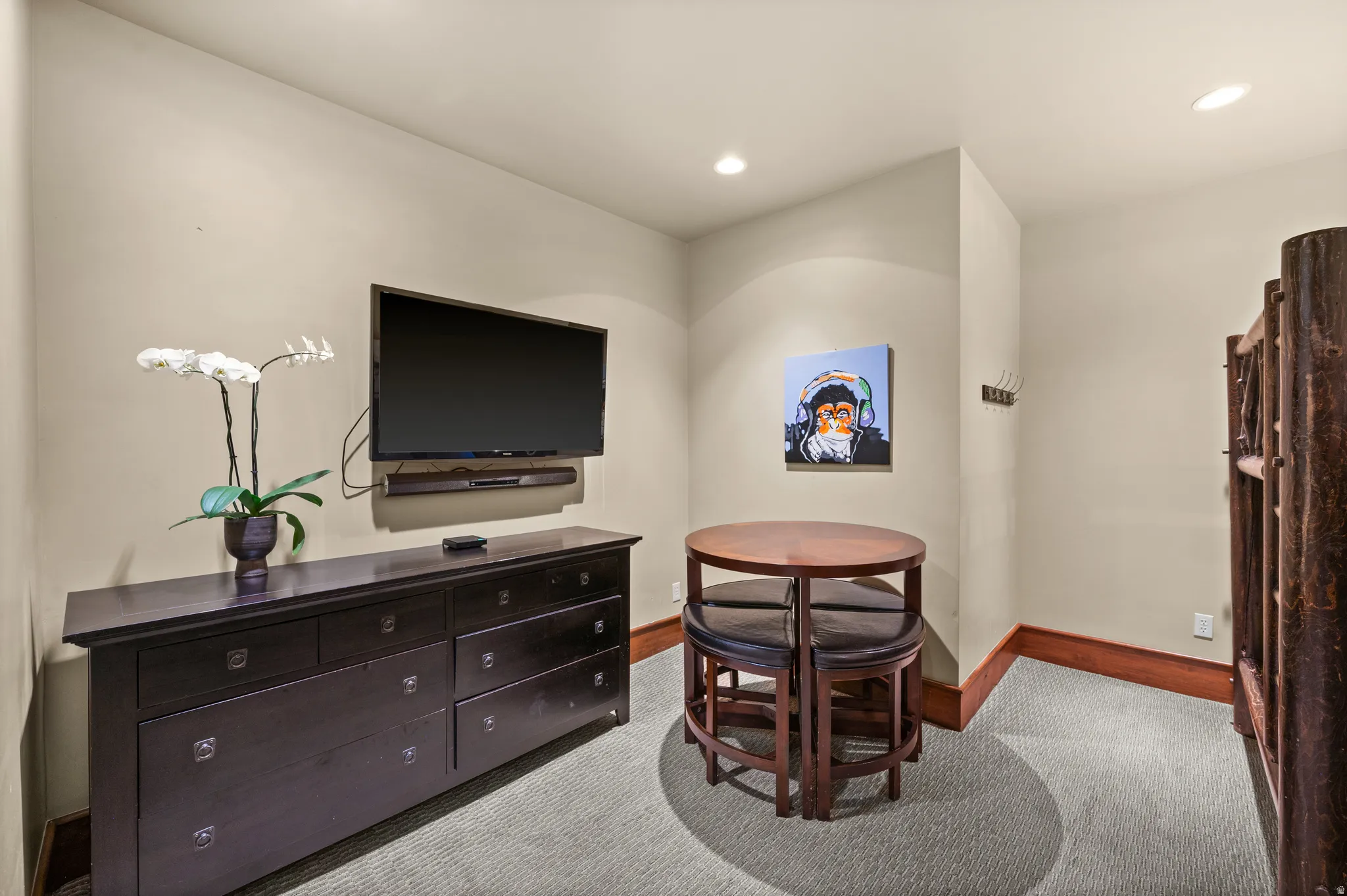Wall-mounted television with soundbar, built-in dresser with multiple drawers, light-colored carpeting, recessed lighting, and wood baseboards