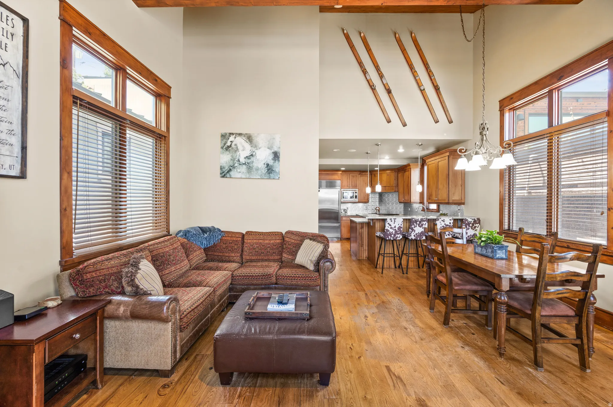 Open-concept living area featuring wood-finish flooring, high ceilings with exposed beams, and substantial window frames