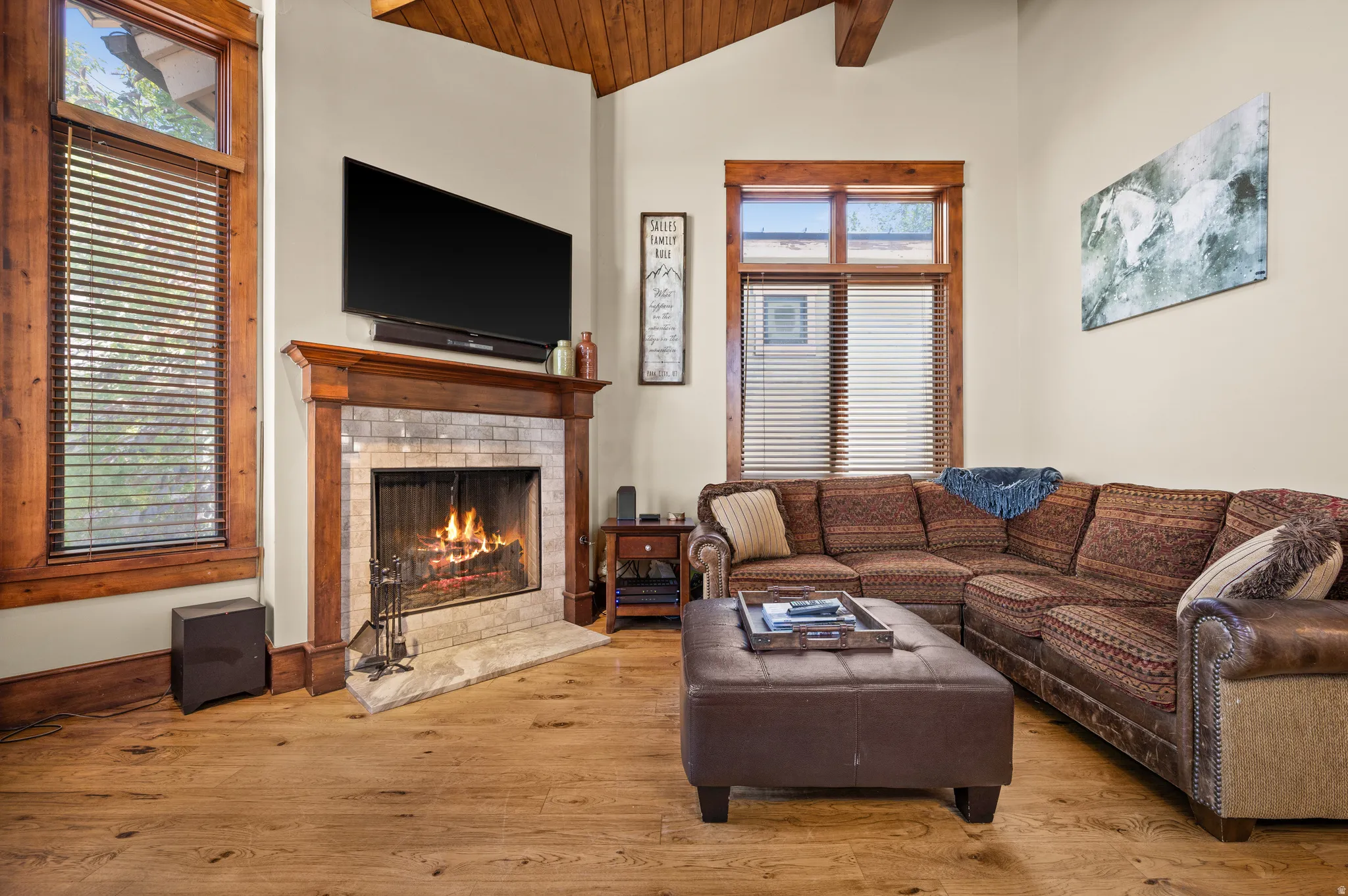 Living area featuring a tiled fireplace with wood mantel, vaulted wood-paneled ceiling, two large windows with wood trim, and wood-finish flooring